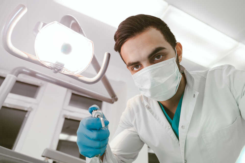 Młody lekarz stomatolog podczas zabiegu oczyszczania zębów u pacjenta
